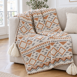 Plaid de canapé à motif géométrique bohème crème, caramel et gris à pompons posé sur un canapé en lin beige