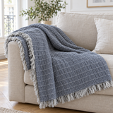 Plaid de canapé en gaze de coton gris ardoise surpiqué à franges posé sur un canapé en lin beige